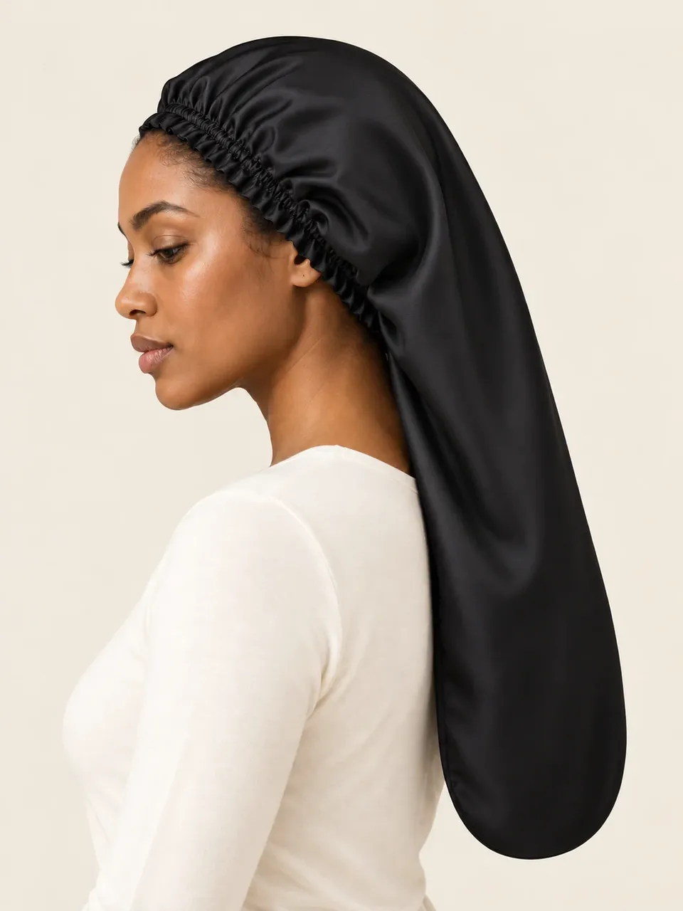 A woman with her hair tucked into a long black silk sleep bonnet, in profile