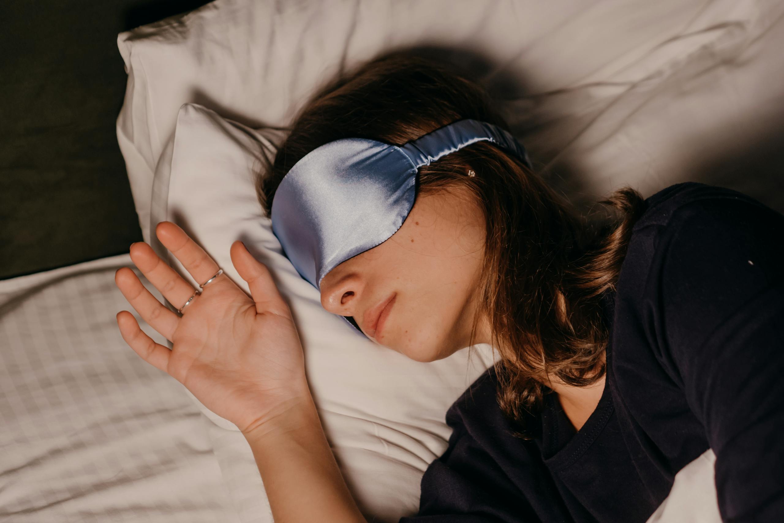 A woman rests peacefully indoors wearing a blue silk sleep mask.